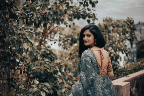 Looking for a sari Portrait of a smiling woman in traditional dress posing in a lush garden setting.