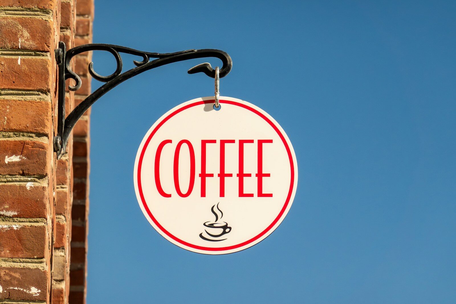 Wishing wanting A round coffee sign hangs on a brick wall.